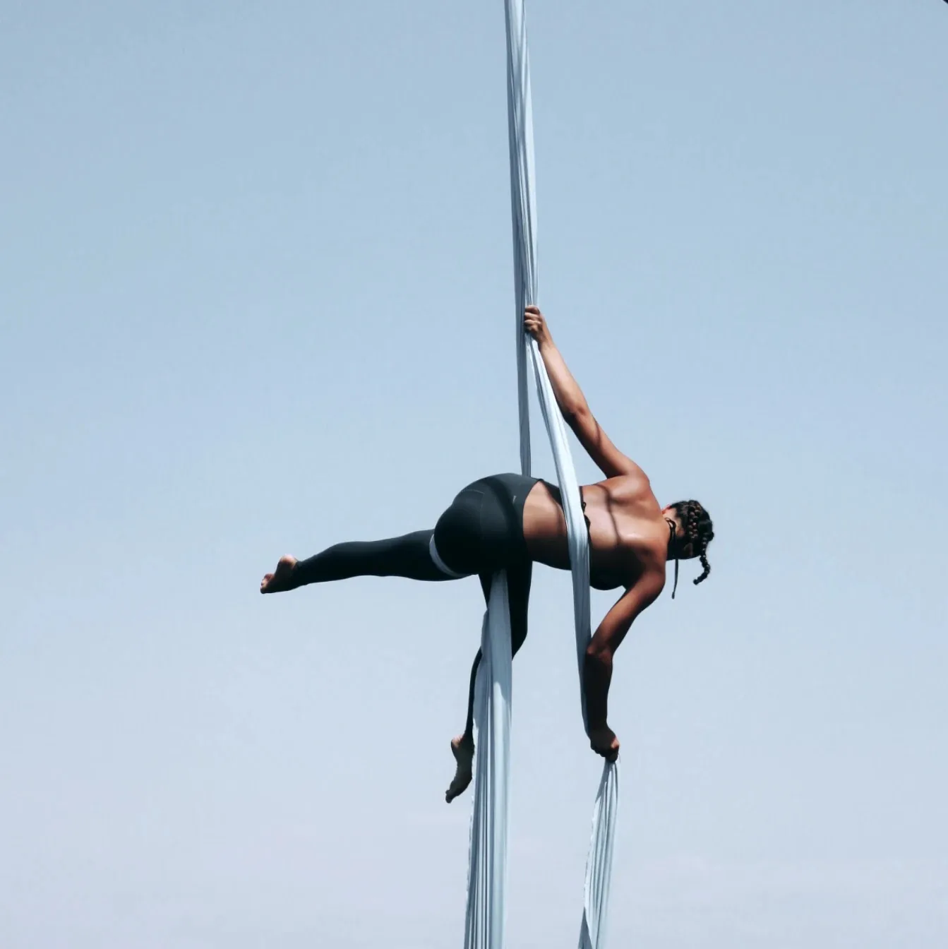 Horizontal pose held on a single white silk against a pale sky