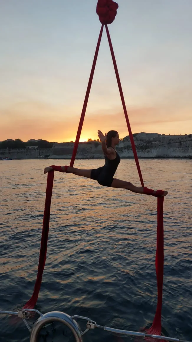 Seated pose on red silks rigged over the sea at sunset