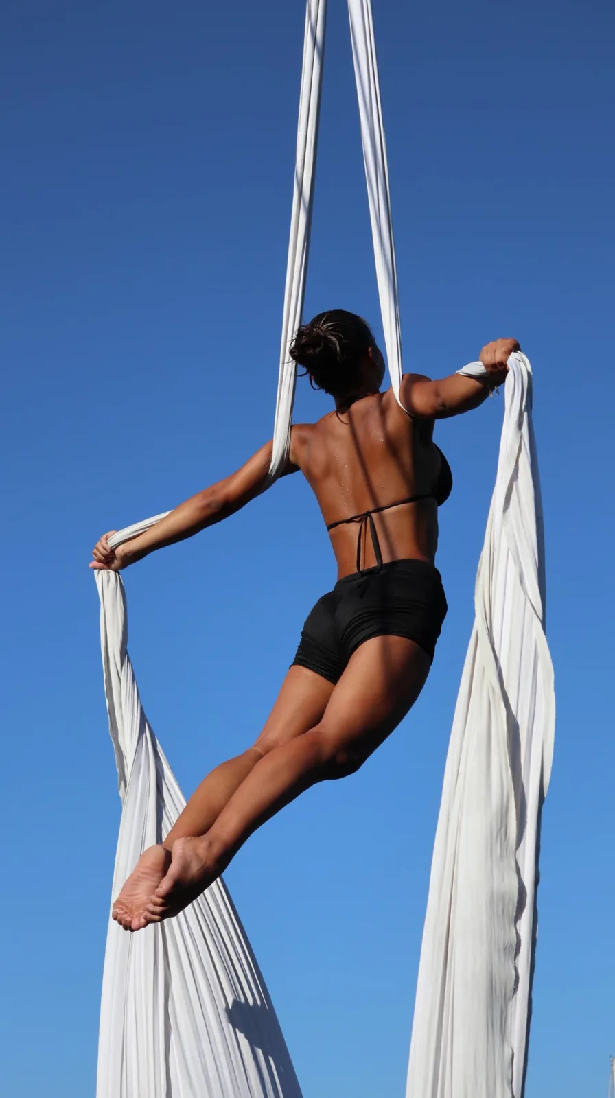 Seen from behind, holding the white silks wide open against a clear blue sky