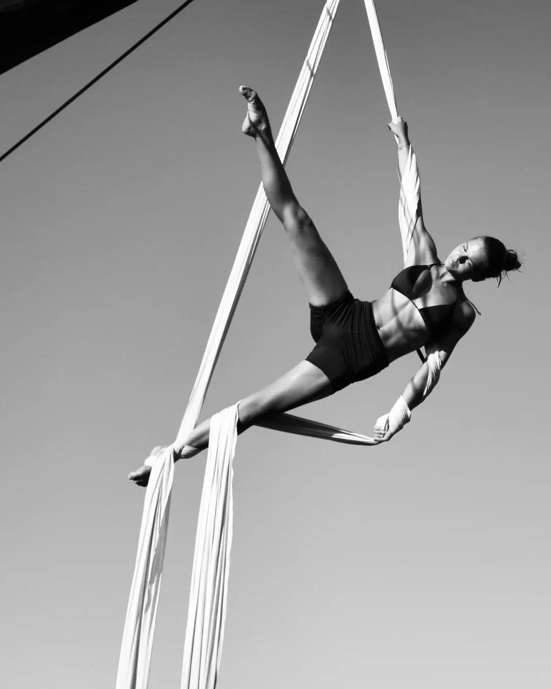 Extended pose held on white silks, photographed in black and white