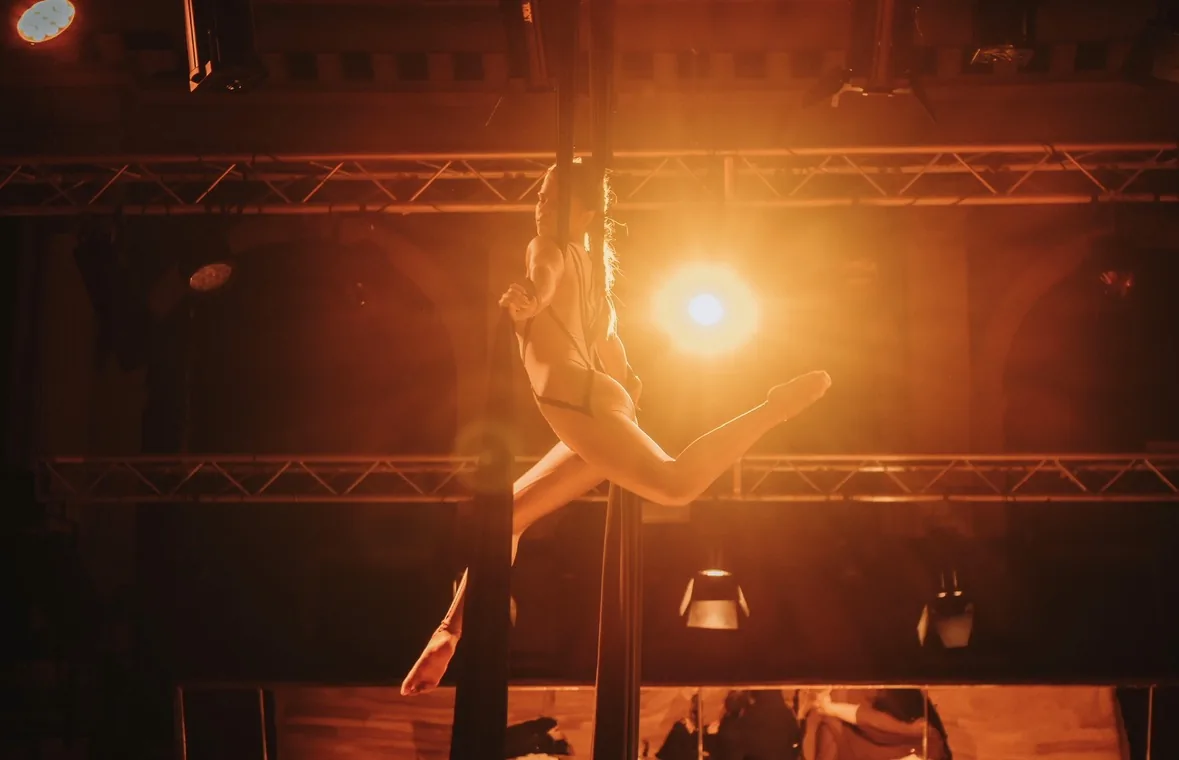Backlit performance on silks under a stage light and rigging truss