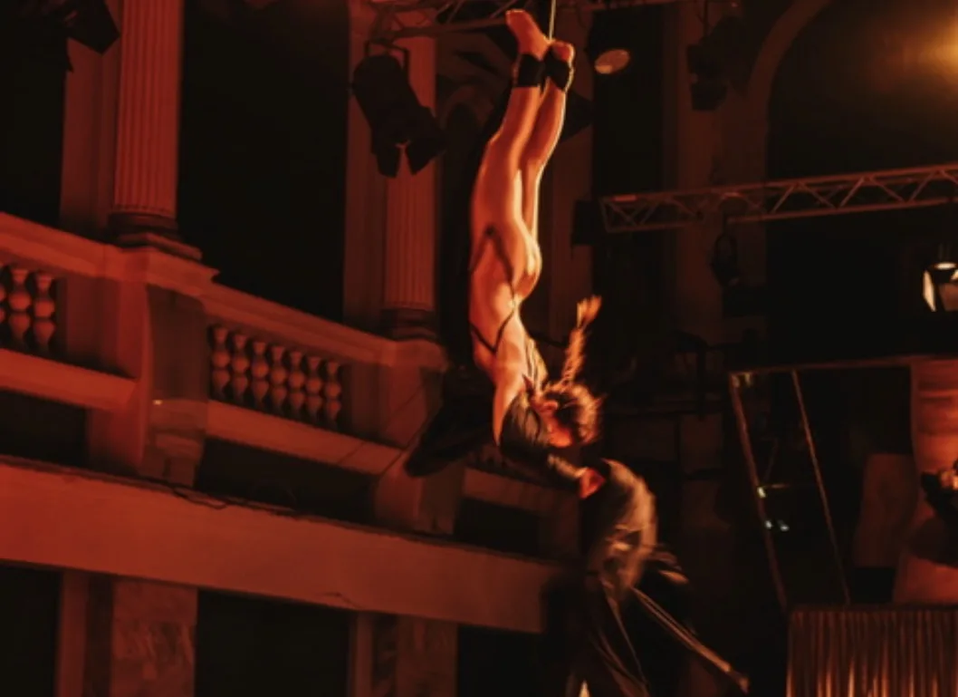 Aerial silks act high in an ornate hall, warm stage light on the architecture